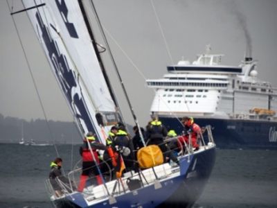 Im Vordergrund segelt eine High-Tech-Segelyacht in leichter Schräglage. Im Hintergrund sieht man ein Kreuzfahrtschiff - die Color Line-, das auf die Yacht zusteuert.