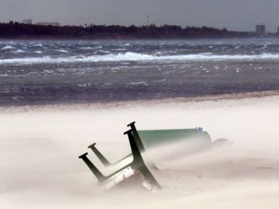 Am Strand liegt eine umgekippte Bank. Drurch einen Sandsturm ist die Bank fast mit Sand bedeckt.