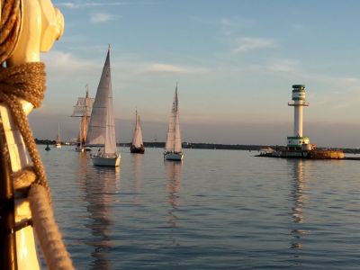 Das Wasser der Ostsee ist spiegelglatt. Es ist Abenddämmerung. Einige Segelschiffe mit gesetzten Segeln selgeln am Friedrichsorter Leuchtturm vorbei.