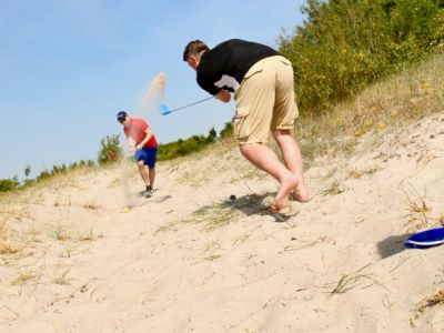 Ein Mann spielt Cross-Golf am Strand und schlägt dabei mit einem Schläger einen Ball über den Sand.